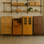 A furniture showroom featuring four wooden cabinets in oak, cherry, and walnut finishes, each with unique drawer and door configurations, displayed beneath minimalist wall shelving with decor items.