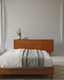 A cherry wood Alano chest of drawers stands against a gray wall, facing the foot of a cherry wood bed with white and gray bedding in a Mid-Century Modern bedroom.