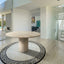 Round solid beige travertine table with fluted travertine legs situated in a luxurious multi floor home